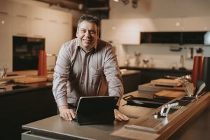 Lächelnder Geschäftsmann mit Laptop am Schreibtisch bewirbt FiberPLUS für Kleinunternehmer