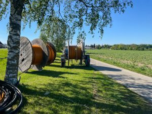 Kabeltrommeln mit orangen Glasfaserkabeln stehen auf Wiese neben Landstraße beim Glasfaserausbau