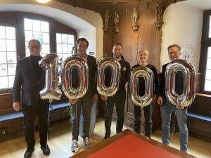5 Vertreter halten Luftballon mit der Zahl 10.000