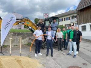 Das Stiegeler Netzbauteam und Vertreter der Tiefbaufirma zusammen mit dem Hilzinger Bürgermeister Holger Mayer und Mitgliedern des Ortschaftsrats vor einem Bagger und Erdhaufen beim Spatenstich für den Glasfaserausbau in Binningen.