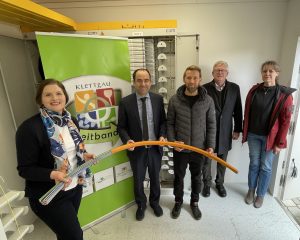 Feierliche Eröffnung des Glasfasernetzes: Fünf Personen halten orangener Rohrverband im neuen Technikstandort
