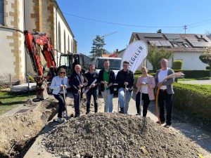 Symbolischer Spatenstich für Glasfaserverlegung mit Vertretern und Bagger im Hintergrund