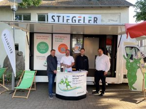 Vier Stiegeler-Mitarbeiter stehen am Infostand vor dem Stiegeler Info-Mobil, um Kunden zu beraten.