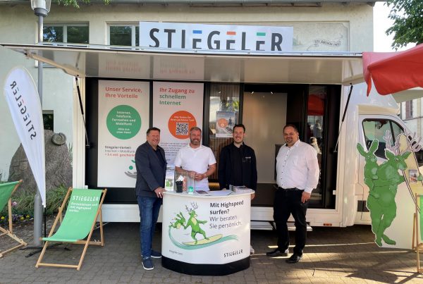 Vier Stiegeler-Mitarbeiter stehen am Infostand vor dem Stiegeler Info-Mobil, um Kunden zu beraten.