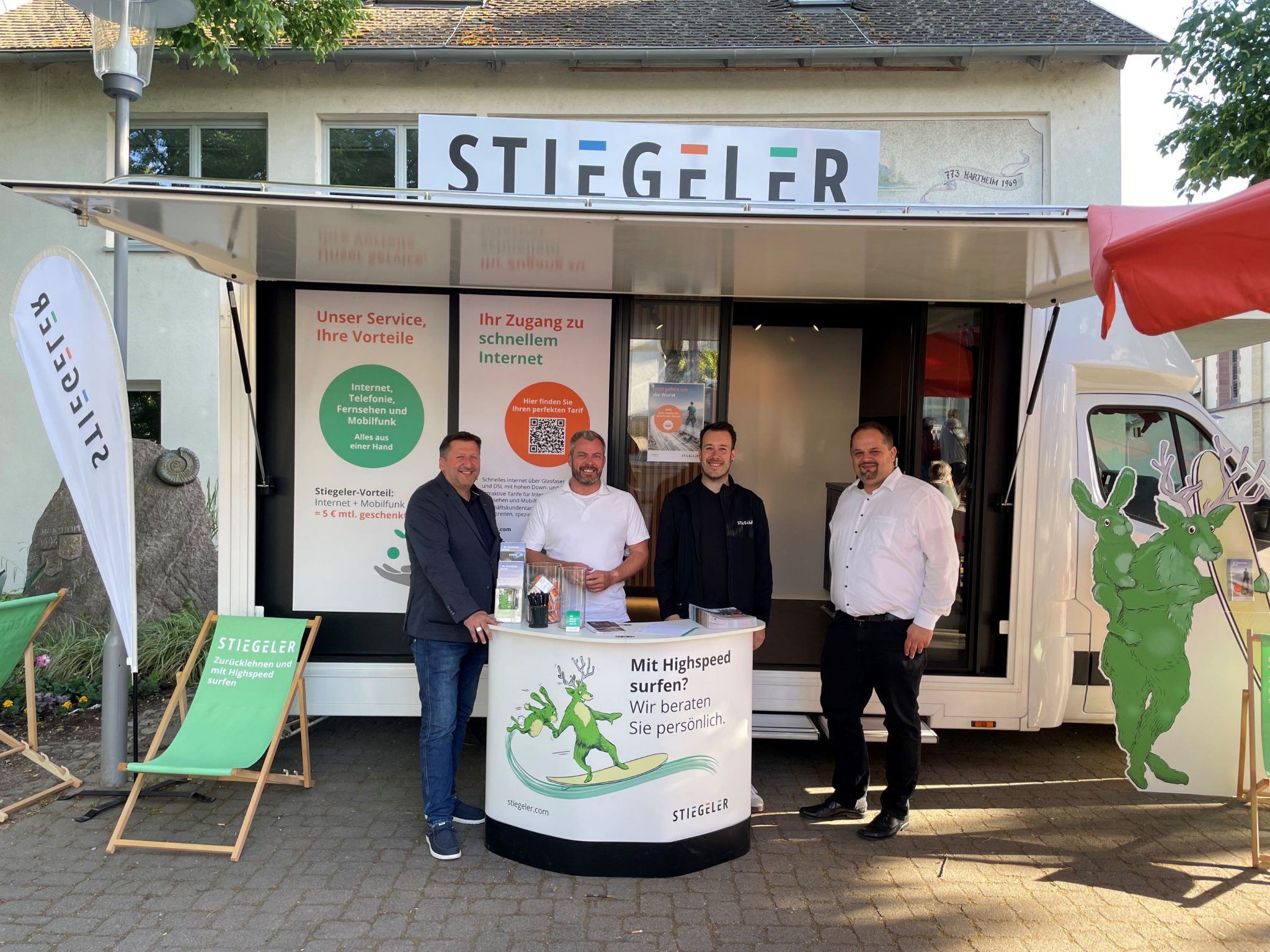 Vier Stiegeler-Mitarbeiter stehen am Infostand vor dem Stiegeler Info-Mobil, um Kunden zu beraten.