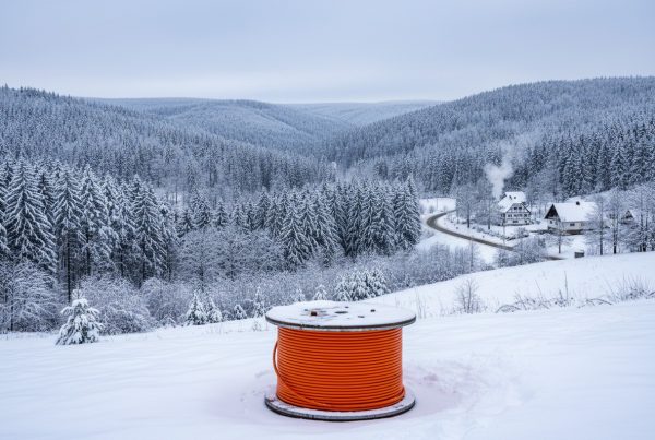 Das Bild zeigt eine orangefarbene Glasfaser-Kabeltrommel in einer verschneiten Schwarzwald-Landschaft.