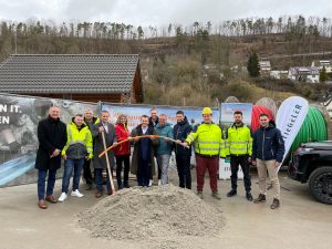 Symbolischer Spatenstich für Glasfaserverlegung mit Vertretern und Kabeltrommel im Hintergrund