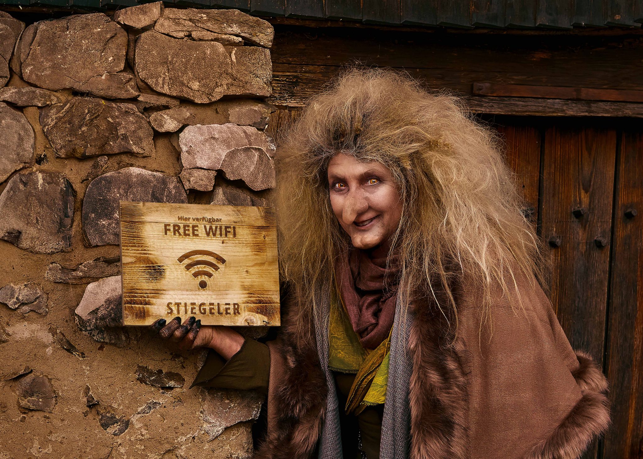 Das Bild zeigt das Key Visual der Stiegeler Markenkampagne "Keine Märchen": Eine Hexe zeigt vor einem Hexenhäuschen ein Schild mit der Aufschrift "Free Wifi".