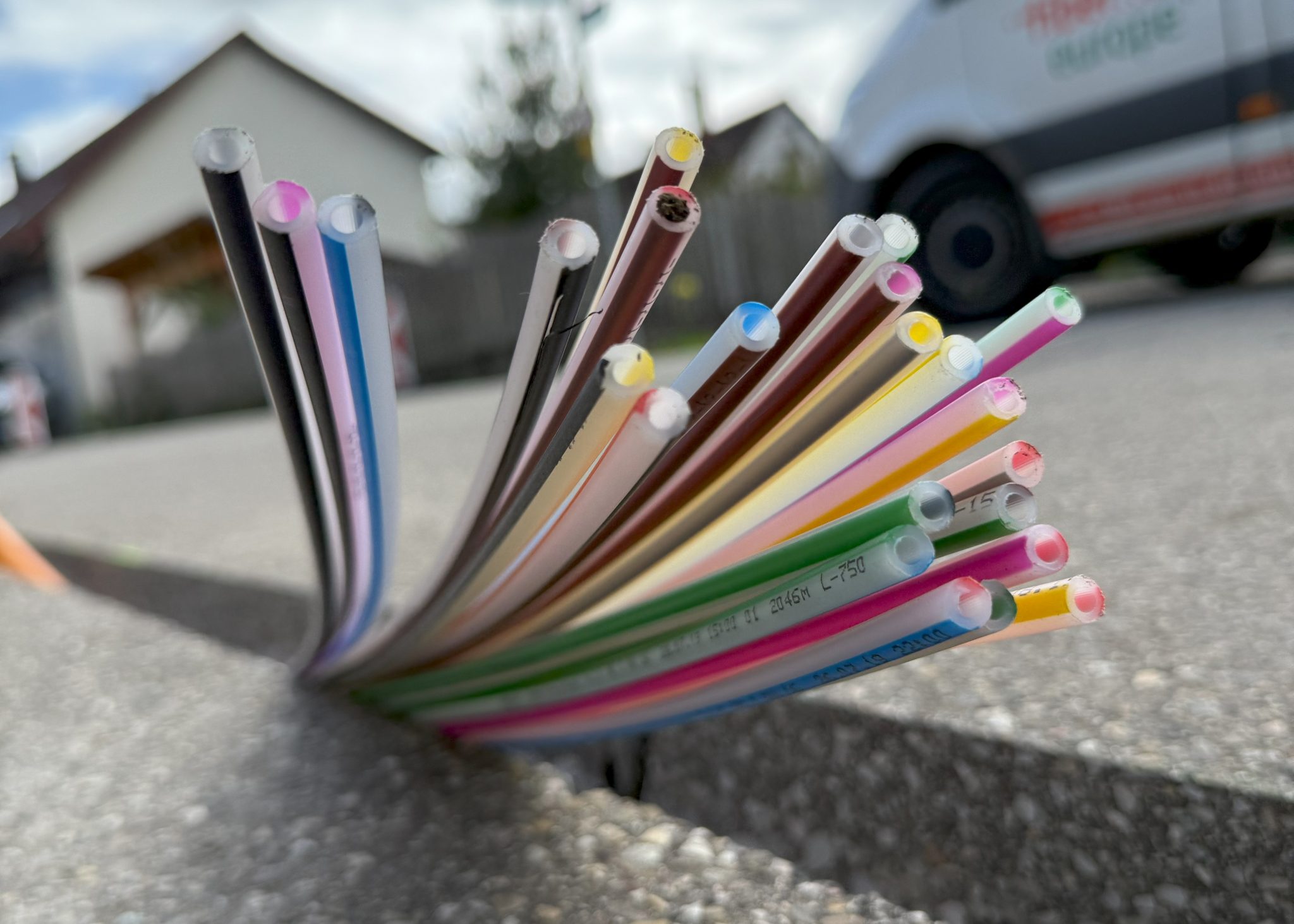 Ein schmaler Spalt in der Asphaltoberfläche einer Straße in Laufenburg, der mit dem Stufenschleifverfahren geschliffen wurde. Aus dem Spalt ragt ein buntes Bündel Leerrohre für die Verlegung von Glasfaserkabeln.